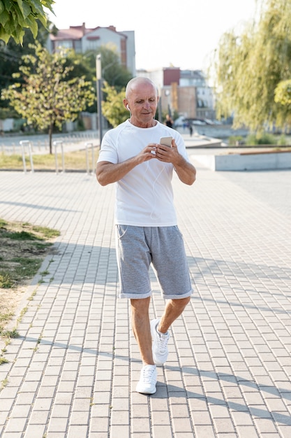 Volledige shot oudere man lopen kijken naar zijn telefoon