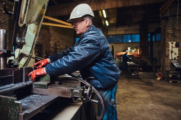 Gratis foto volwassen ervaren werknemer snijdt metaal met behulp van een speciale werktuigmachine.