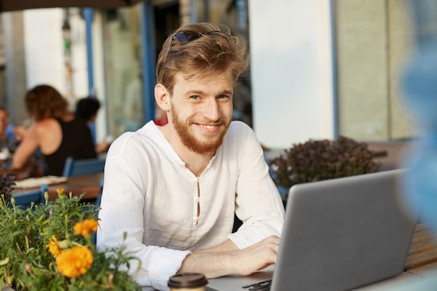 Volwassen gember knappe man met laptopcomputer zittend op het terras van een restaurant of café