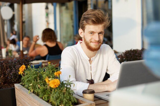 Volwassen gember knappe man met laptopcomputer zittend op het terras van een restaurant of café