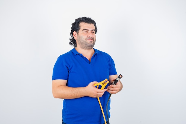 Volwassen man bouwgereedschap in blauw t-shirt te houden en op zoek attent. vooraanzicht.