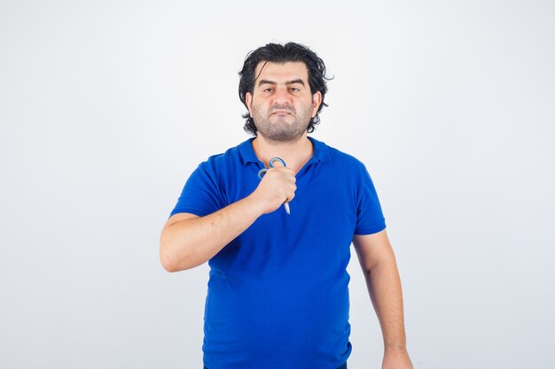 Volwassen man met schaar, lippen tuit in blauw t-shirt en op zoek agressief, vooraanzicht.