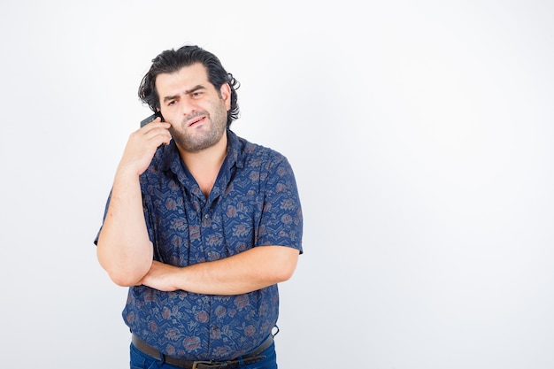 Volwassen man praten op mobiele telefoon in shirt en op zoek verveeld, vooraanzicht.