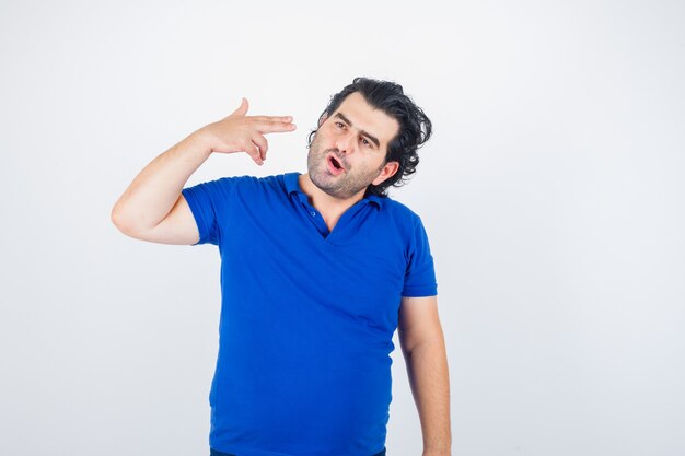 Volwassen man zelfmoordgebaar in blauw t-shirt tonen en peinzend kijken. vooraanzicht.