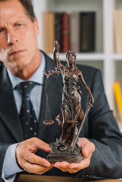 Gratis foto volwassen mannelijke advocaat standbeeld van justitie in de hand te houden