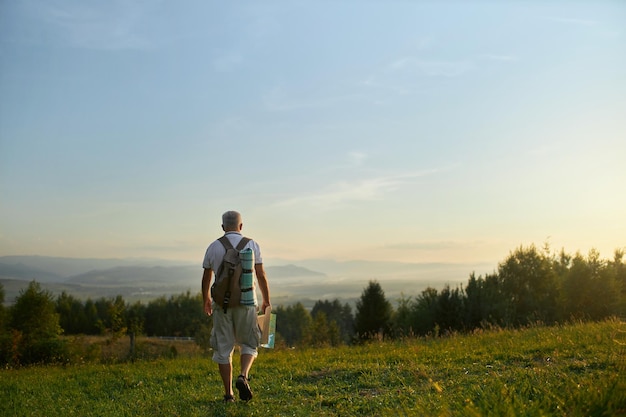 Volwassen mannelijke reiziger die langs een groene heuvel loopt terwijl hij in de bergen backpackt