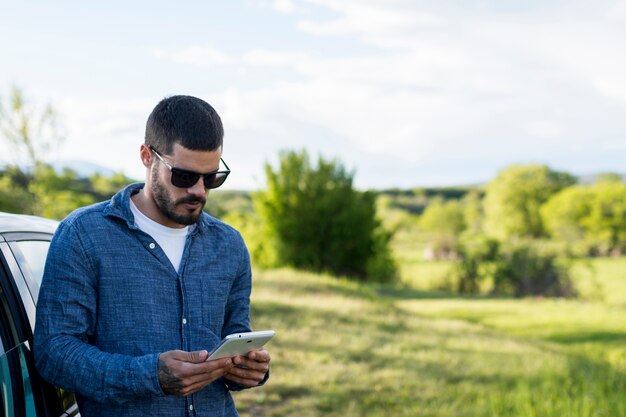 Volwassen mens die op auto leunt en tablet gebruikt