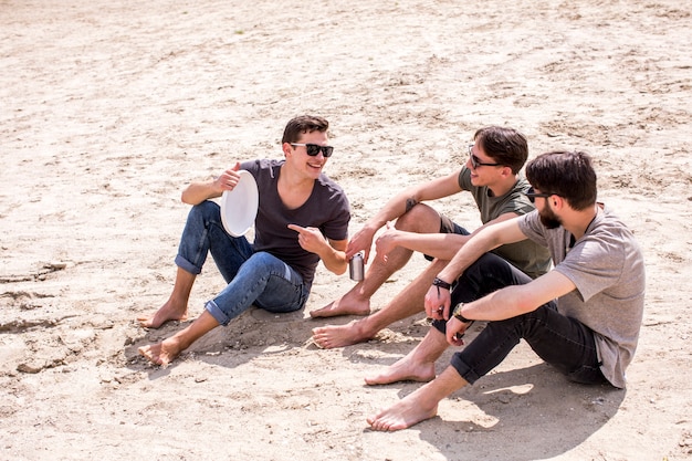 Volwassen mens die speel frisbee vrienden aanbiedt die op strand zitten