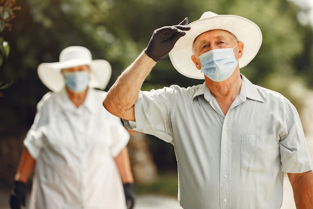 Volwassen paar in een zomertuin. Coromavirus-thema. Mensen met een medisch masker. Knappe oudste in een wit overhemd.