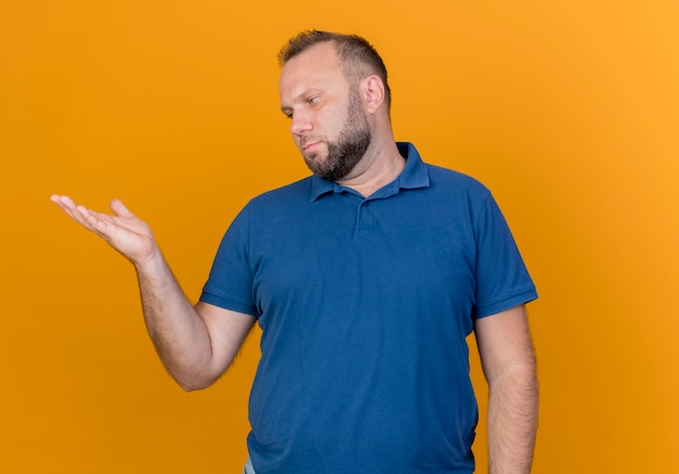 Volwassen Slavische mens die lege hand toont en bekijkt geïsoleerd op oranje muur