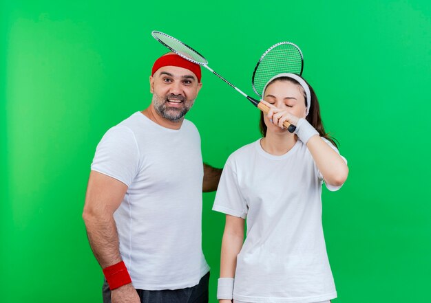 Volwassen sportieve paar dragen hoofdband en polsbandjes houden badmintonrackets onder de indruk man op zoek en vrouw raakt zijn hoofd met racket met gesloten ogen