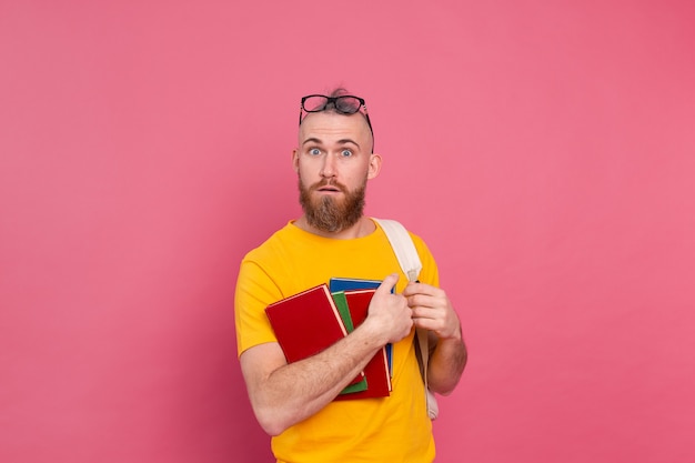 Volwassen student vrolijke vrijetijdskleding man met baard en rugzak met boeken geïsoleerd op roze