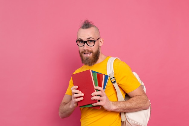 Volwassen student vrolijke vrijetijdskleding man met baard en rugzak met boeken geïsoleerd op roze