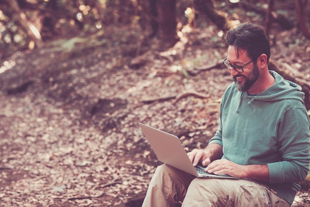 Volwassen volwassen man gebruikt laptopcomputer met roaming internetverbinding in het midden van het bos - concept van externe werknemer en slim werkende moderne mensen - knappe man geniet van draadloze nieuwe baan