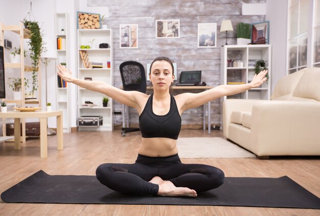 Volwassen vrouw die ontspanning beoefent terwijl ze in yoga lotus pose zit in de woonkamer.