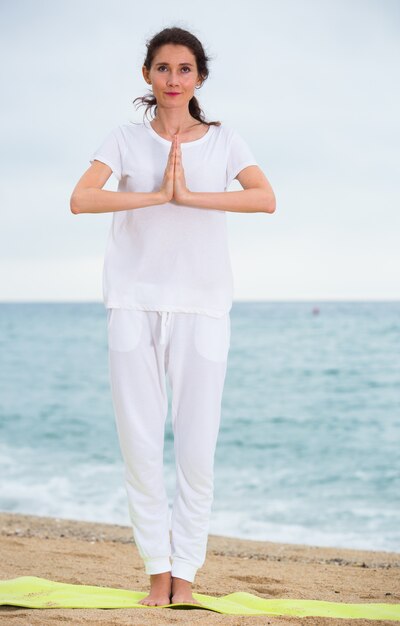 Volwassen vrouw in wit T-shirt blijft en oefent asana