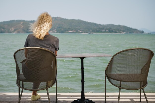 Volwassen vrouw zit alleen op een stoel voor de zee met een gevoel van eenzaamheid naast een lege stoel het idee van verlies en selectieve aandacht voor geestelijke gezondheid