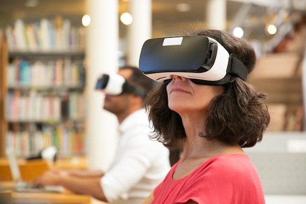 Volwassen vrouwelijke student die op virtuele videoleerprogramma in bibliotheek letten