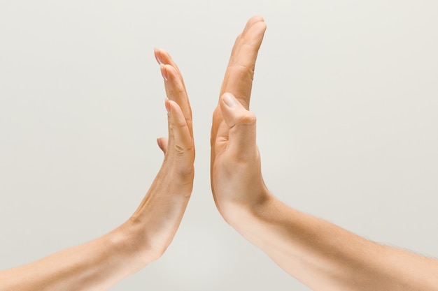 Voor altijd vrienden. Mannelijke en vrouwelijke handen die een gebaar van het krijgen van aanraking of groeten demonstreren die op grijze studioachtergrond worden geïsoleerd. Concept van menselijke relaties, relatie, gevoelens of zaken.