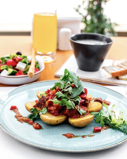 Gratis foto vooraanzicht aardappelen met vlees in tomatensaus met rucola en griekse salade op tafel