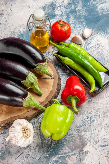 Vooraanzicht aubergines op boom houten bord hete pepers op zwarte plaat knoflook groene en rode paprika's tomaat fles olie op blauw-witte achtergrond