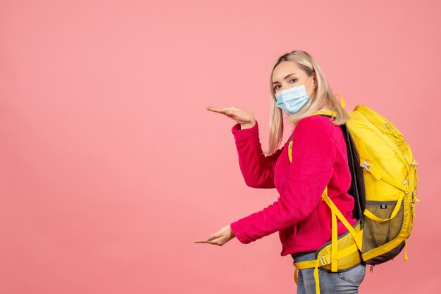 Vooraanzicht blonde reizigersvrouw met gele rugzak die masker draagt dat grootte met handen toont