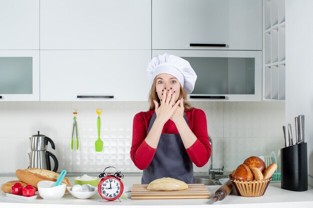 Vooraanzicht blonde vrouw in kok hoed en schort handen op haar gezicht in de keuken zetten