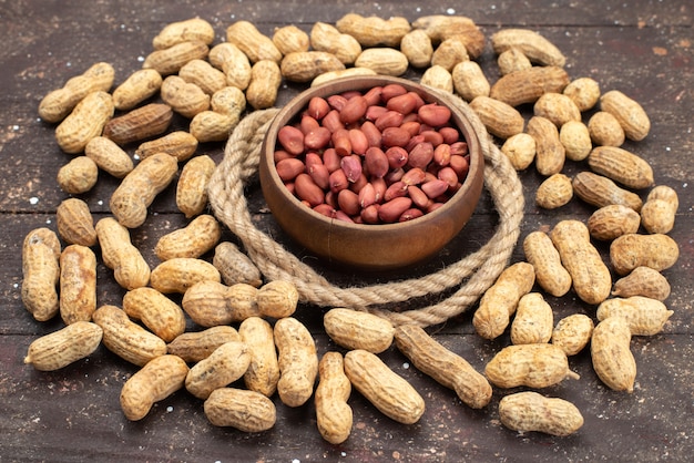 Vooraanzicht bruine rauwe noten in ronde kom met touwen en gele noten op het bruine achtergrond noten walnoot snack zout