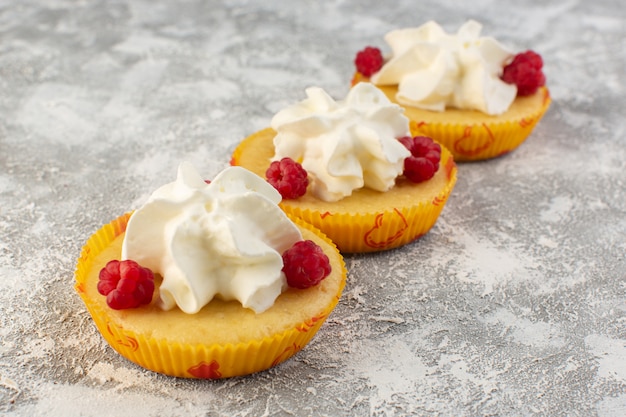 Gratis foto vooraanzicht cakes met room lekker gebakken ontworpen met framboos op het grijze bureau