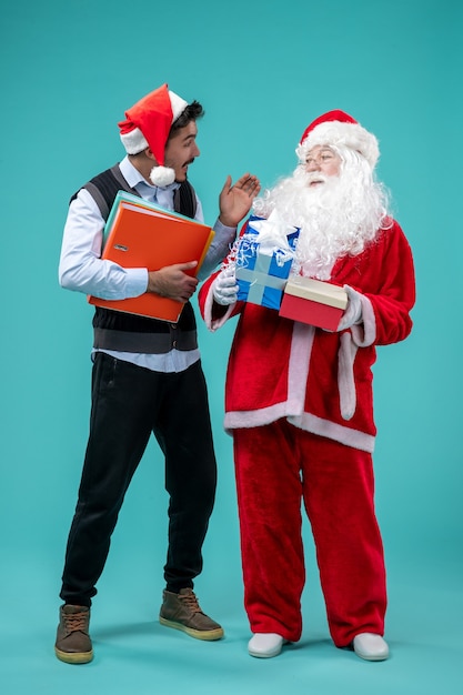 Gratis foto vooraanzicht de kerstman met jong mannetje en stelt op blauw bureau voor