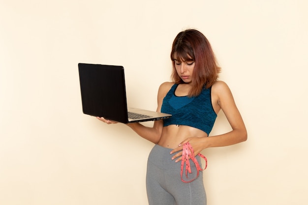 Vooraanzicht die van jong wijfje met geschikt lichaam in blauw overhemd haar laptop op witte muur houden