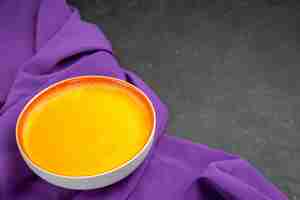 Gratis foto vooraanzicht eenvoudige pompoensoep op paars weefsel en donkere tafel