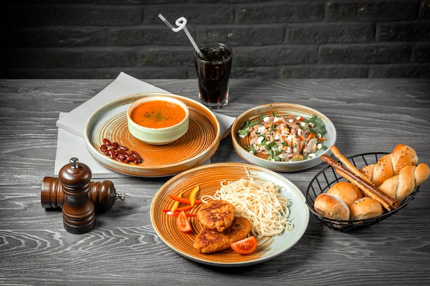 Vooraanzicht eerste tweede en hoofdgerecht linzensoep salade en schnitzels met pasta en een frisdrank op tafel