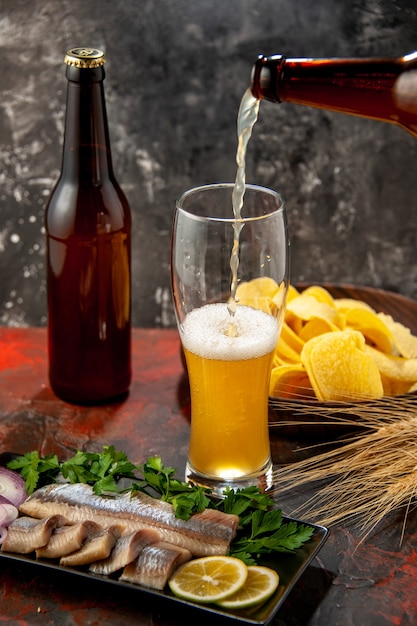 Vooraanzicht fles beer die in het glas stroomt met cips en vis op een lichte achtergrond