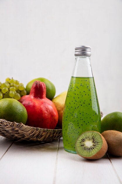 Vooraanzicht fles groen sap met granaatappels druiven, mandarijnen en peer in een mand op een witte muur