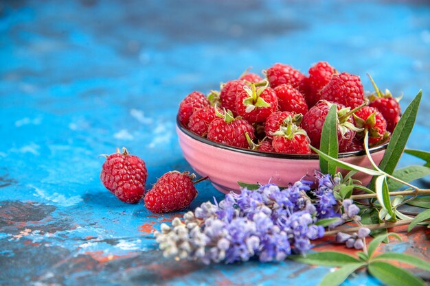 Vooraanzicht frambozen in een kom paarse bloemen op blauwe tafel vrije plaats