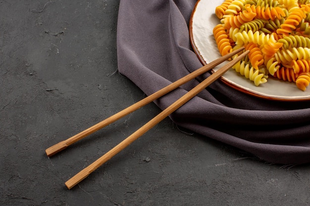 Gratis foto vooraanzicht gekookte italiaanse pasta ongebruikelijke spiraal pasta binnen plaat op de donkere ruimte