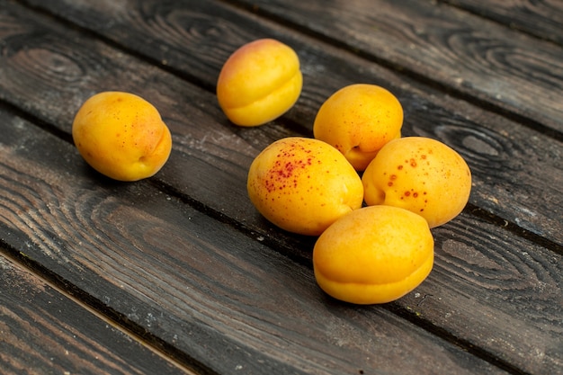 Gratis foto vooraanzicht gele abrikozen zacht en vers fruit op het bruine rustieke bureau