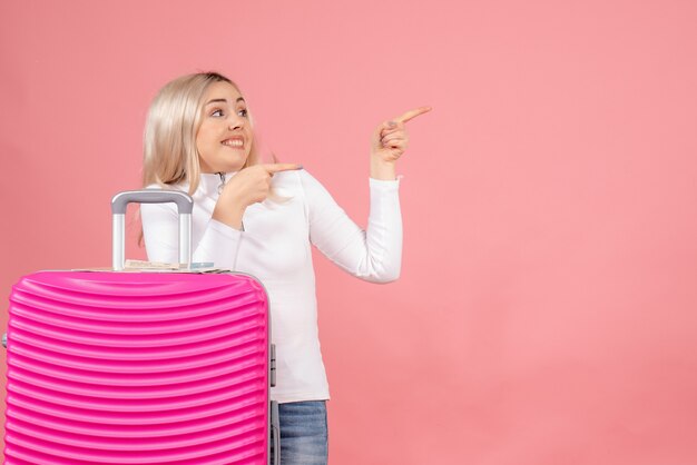 Vooraanzicht gelukkig mooie vrouw met roze koffer naar rechts wijzend