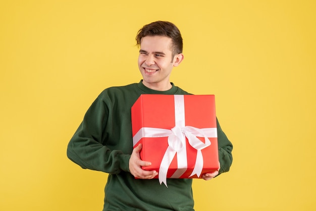 Vooraanzicht gelukkige jonge man met groene trui kerstcadeau op geel te houden