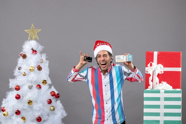 Vooraanzicht gelukkige jonge man met kaart en reisticket rond kerstboom
