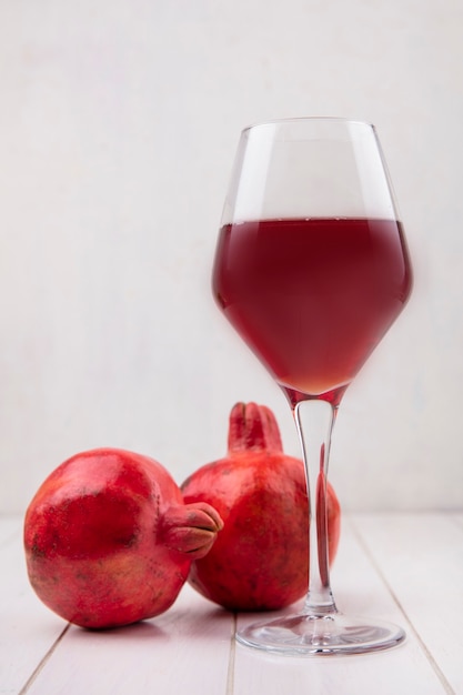 Vooraanzicht glas granaatappelsap met granaatappels op witte muur