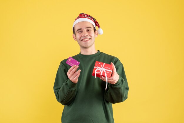 Vooraanzicht glimlachte jonge man met kerstcadeau staande op geel