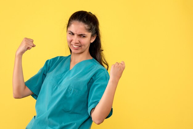 Vooraanzicht glimlachte vrouwelijke arts die haar geluk toont die zich op gele achtergrond bevindt