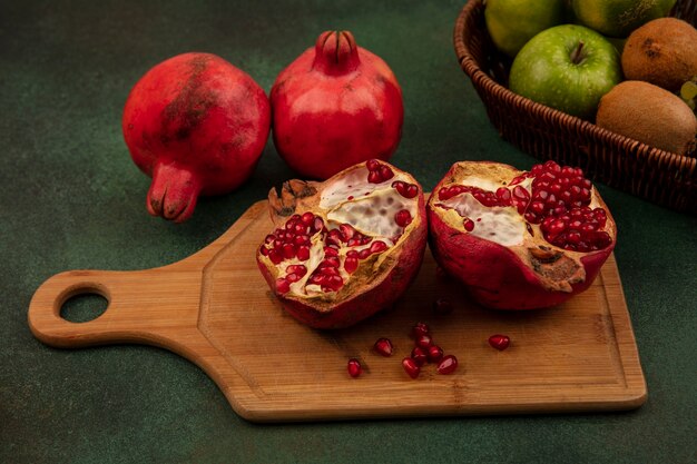 Vooraanzicht granaatappels op een snijplank met kiwi en appels in een mand op een groene muur