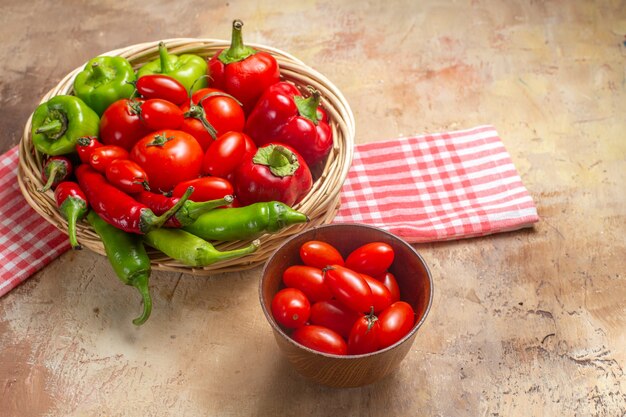 Vooraanzicht groene en rode paprika's hete pepers tomaten in rieten mand cherry tomaten in kom keukenhanddoek op amberkleurige achtergrond met vrije ruimte
