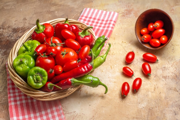 Vooraanzicht groene en rode paprika's hete pepers tomaten in rieten mand verspreide kerstomaatjes uit kom keukenhanddoek op amberkleurige achtergrond