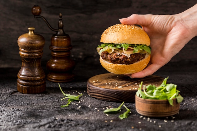 Vooraanzicht hand met rundvlees hamburger met salade en spek