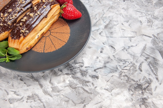 Gratis foto vooraanzicht heerlijke choco-eclairs met aardbeien op lichte vloercakedessertkoekje