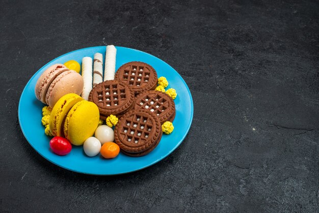 Vooraanzicht heerlijke Franse macarons met snoepjes en chocoladekoekjes op grijs oppervlak biscuit suiker cake zoete koekjes bakken